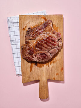 Cooked beef steak on wooden board with pink background