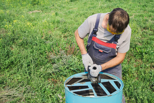 Worker using an angle grinder to cut metal barrel for DIY upcycling project