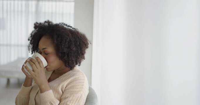 Portrait of young beautiful African American black woman hands holding coffee cup morning spring time in white bedroom. Happy cheerful relaxing in winter. Wakeup university lifestyle concept.