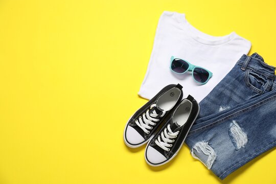 Stylish child's clothes, sunglasses and shoes on yellow background, flat lay. Space for text