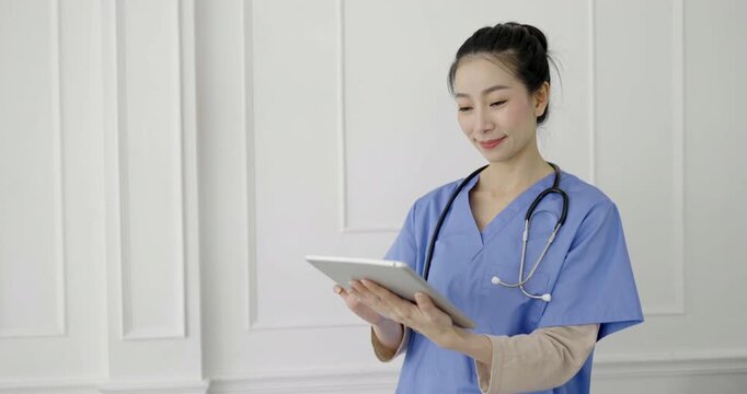  Asian doctor holding ipad gadget in medical office. Doctor intern woman checking information.