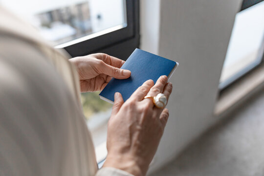 Hands holding blue passport near window before travel