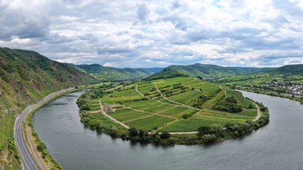 Weitwinkel-Luftaufnahme der berühmten Moselschleife mit der historischen Klosterruine Stuben auf einer von grünen Weinbergen geprägten Halbinsel unter bewölktem Himmel. © fotoping