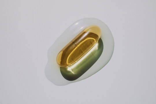 Golden gel capsule in clear liquid puddle on light background
