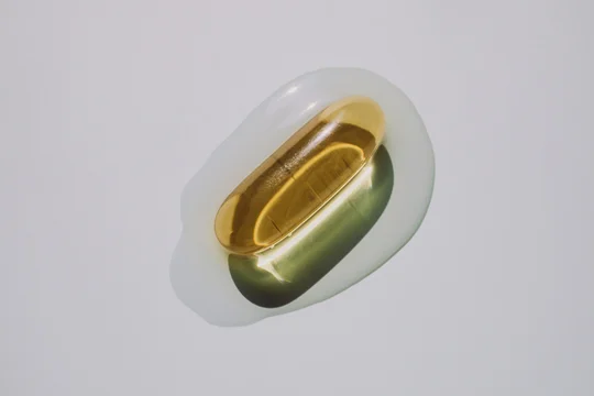 Golden gel capsule in clear liquid puddle on light background