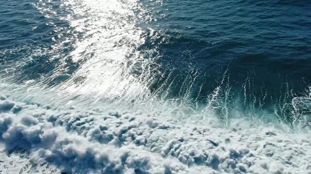 Aerial view of crashing ocean wave with sun glint and sea foam, high-definition tropical blue water surface background, for cinematic travel projects