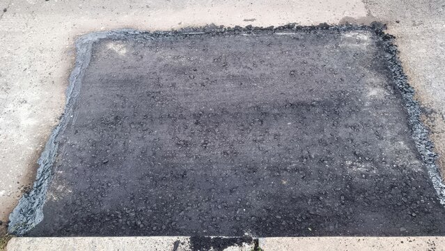 Fresh asphalt patch on concrete surface with rough texture and dark gray tones