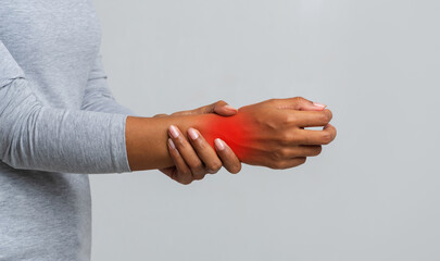 Fototapeta premium Cropped image of African American woman suffering from rheumatism, massaging her wrist, grey background