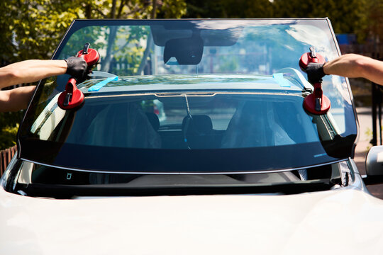 Professional technicians carry new auto glass equipped with vacuum lifters towards the car to complete the outdoor mobile window installation