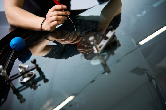 Expert mechanic performs a final glass fracture inspection using a scriber tool for damage finishing during a professional windshield crack repair service