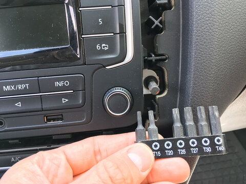 Hand holding Torx bits near a car radio with mix rpt and info buttons in the dashboard.