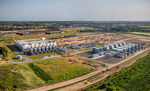 Panorama view of a modern data center complex with adjacent energy infrastructure, utility facilities, and expansion areas under construction within a large industrial park