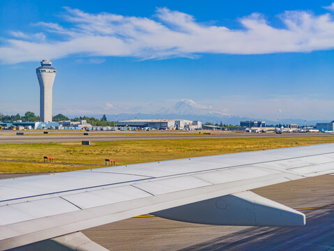 Airplane wing view of airport control tower and Mount Rainier