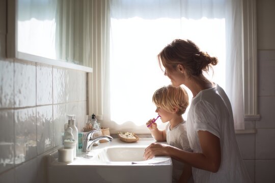 Bright minimalist bathroom with parent and young child brushing teeth side by side at sink, soft morning light streaming in. Family hygiene routine, parenting moment.
