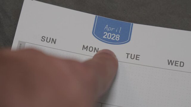 finger pointing at April 2028 planner page close up for scheduling and monthly planning concept