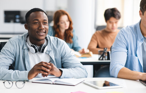 Back To Highschool. Portrait of interested black student sitting at desk with multiracial classmates, listening to teacher. Diverse people studying and learning new stuff, selective focus