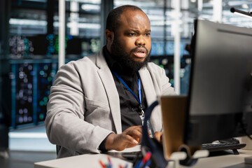 Fototapeta premium African American programmer looks worried after analysis reveals infrastructure failure errors and a network outage in a data center.