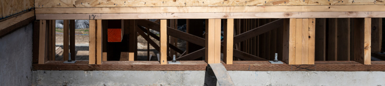 Wood i-beam floor joists installed at new home build, OSB oriented strand board, housing construction project job site, anchor bolts securing solid beam to foundation
