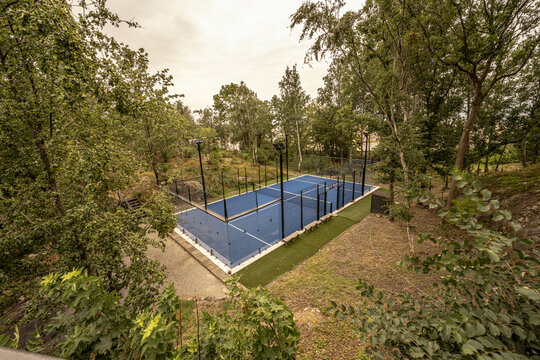 Blue outdoor racket sport court surrounded by trees.