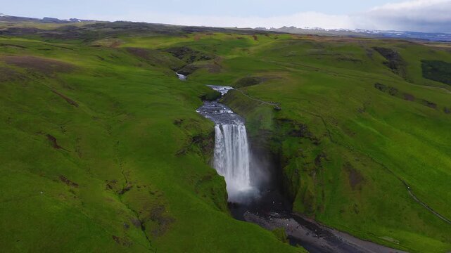 Aerial view of Skogafoss in southern Iceland shows a single plunge, mist, flowing river, upstream cascades, footpath, platform, visitors, and distant peaks.