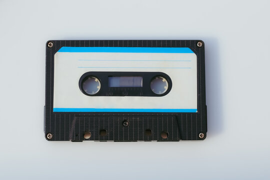 A blank vintage compact cassette tape with a black shell and a white label isolated on white. 1980s 1990s design element. Template with copy space.