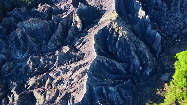 Dramatic aerial view of dark eroded badland topography with sharp ridges and deep shadows, showcasing unique geological formations.