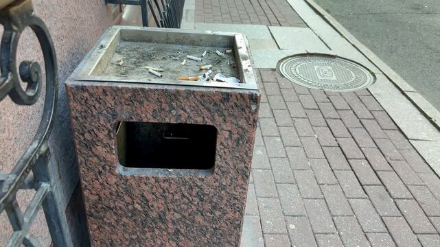 An ashtray-urn made of stone stands in a smoking area outside a business class hotel. Smoked cigarettes are visible inside the urn on the street