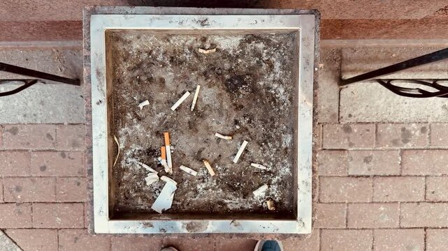 An ashtray-urn made of stone filled with smoked cigarettes stands in the smoking area at the entrance of a business class hotel