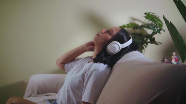 Young woman listening to music on headphones and relaxing on sofa