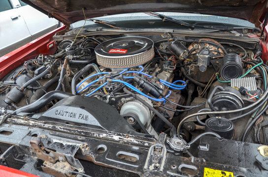 Open hood view of powerful V8 engine compartment of classic 1970s American car with prominent chrome Edelbrock air filter blue spark plug wires and factory radiator setup