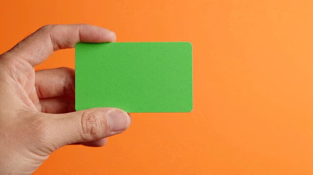 Hand holding a blank green card against an orange background
