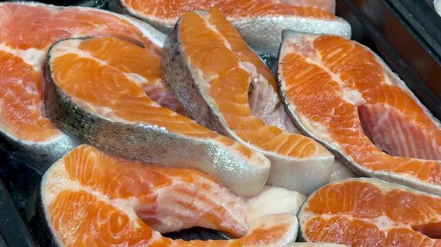 Chilled Atlantic salmon steaks piled, glittering ice crystals on raw orange fillets on black tray, retail display vibe, cold