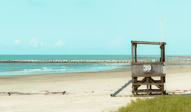 GALVESTON, TEXAS, USA: A wooden beach lifeguard tower displaying the number 39 stands on an empty sandy beach with a stone breakwater jetty and the Gulf of Mexico in the background