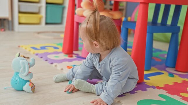 Toddler girl holding plush elephant toy seated on foam puzzle mat in building; gentle curiosity calm.