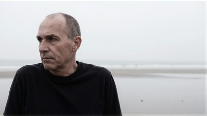 Fototapeta premium Man in black shirt gazes thoughtfully at foggy beach horizon.
