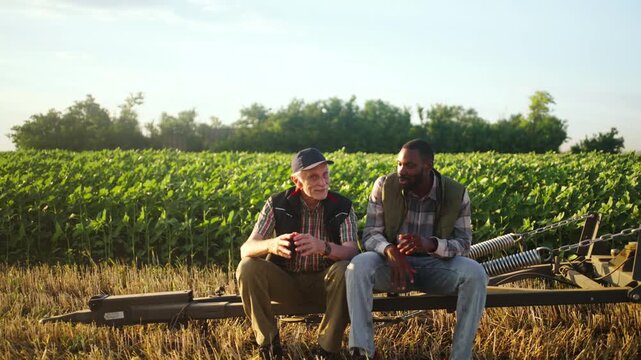 Two agricultural workers taking a break and talking on a farm trailer, showing rural teamwork, farming knowledge and everyday life on the farm.