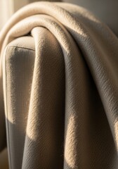 Obraz premium Cozy beige wool blanket draped over comfortable armchair. Soft textile fabric texture in warm natural light. Home interior decor, relaxation, hygge style and lifestyle concept.