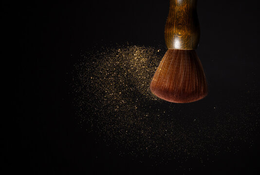 Big Soft Makeup brush with powder explosion. Cosmetic brush splash powder dust with gold glitter sparkling for make up. Black background isolated on photo element
