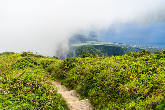 Hiking path leading up Mount Pelee in Martinique, showing a scenic mountain trail with green grass, rolling clouds, and the ocean below