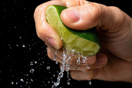 Hand squeezing fresh lime with juice splashing on black background