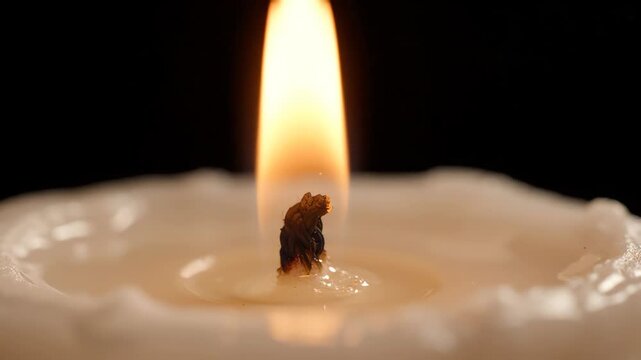 Macro shot of a wax candle wick igniting and burning with a steady golden flame in complete darkness