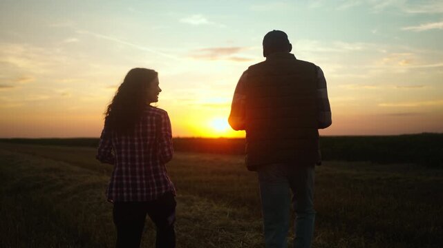 Two agricultural workers walking across a field at sunset, sharing a discussion about farm work, crop growth and countryside lifestyle.