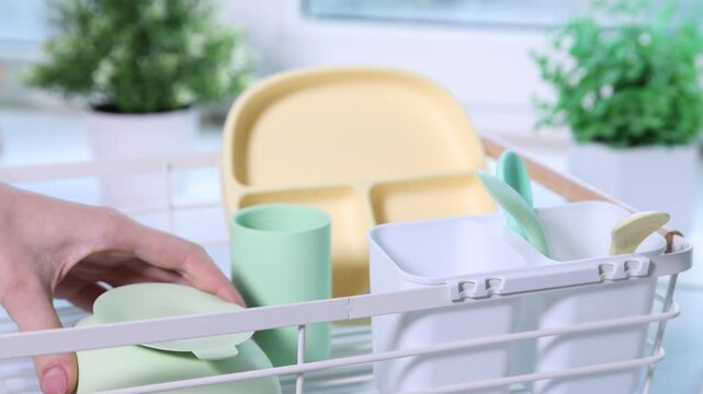Woman putting baby tableware into drying rack in kitchen, closeup