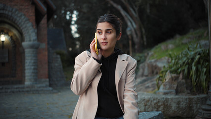 Obraz premium Young Hispanic woman sitting in an urban setting, listening to audio messages on her smartphone with focus and concentration during a modern city moment.