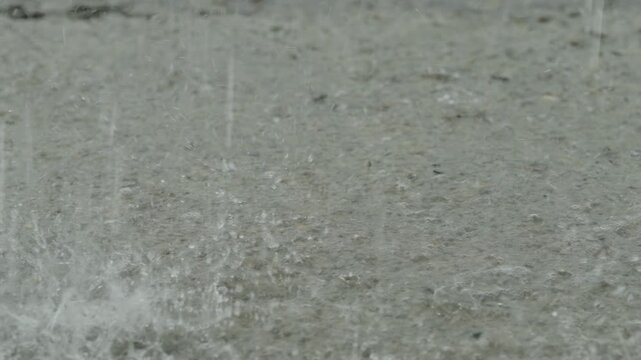 Rain drops falling into a muddy puddle on broken asphalt.