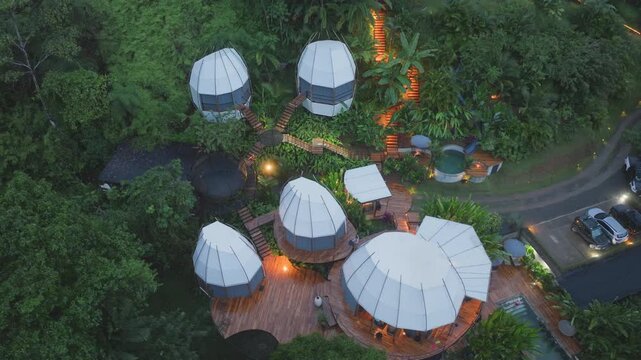 Beautiful villa bungalow in Costa Rica nestled within dense tropical rainforest. Aerial view of geodesic dome accommodations with wooden decks and pool at dusk surrounded by jungle foliage.