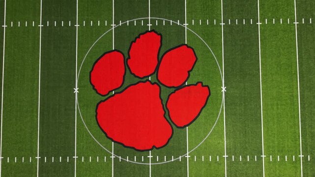 Aerial perspective of a football field showcasing a prominent red paw print logo at the center, surrounded by yard lines and end zones