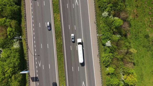 Aerial perspective of a busy highway featuring various vehicles moving along the lanes, bordered by vibrant greenery and trees, illustrating the continuous flow of traffic in a rural setting