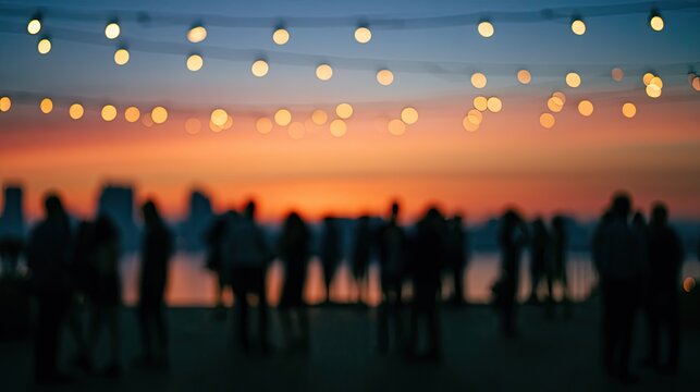 Silhouetted crowd gathers near waterfront at sunset, illuminated by string lights