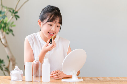 A child, a girl, elementary school or middle school age, applying lipstick and makeup while looking in the mirror.